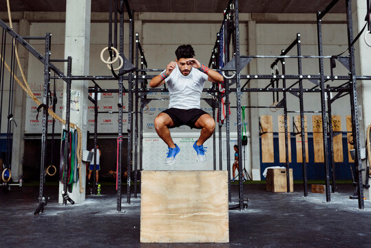 Young athlete exercising box jumps at gym