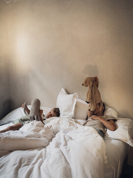 Friends play with plush toy while resting in comfortable bed