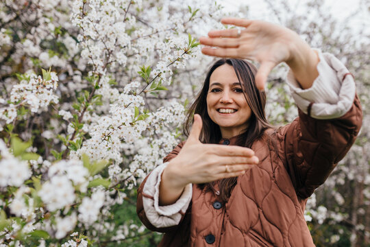 Smiling woman making a finger frame among spring blossom trees