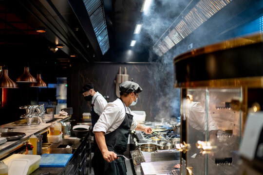 Chefs wearing protective face mask preparing dish in restaurant kitchen