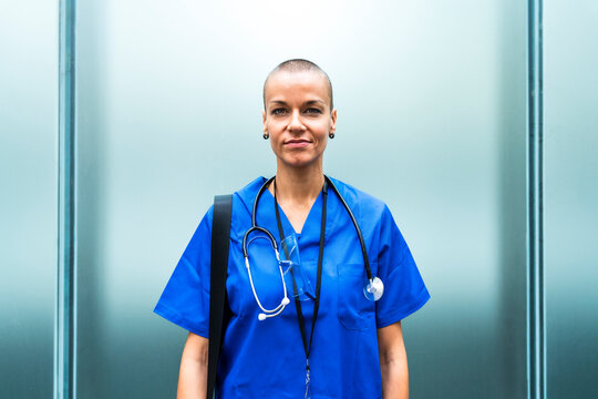 Mature female nurse with stethoscope in front of wall