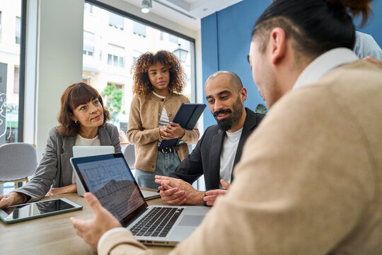 Colleagues discussing blueprint on laptop in office meeting
