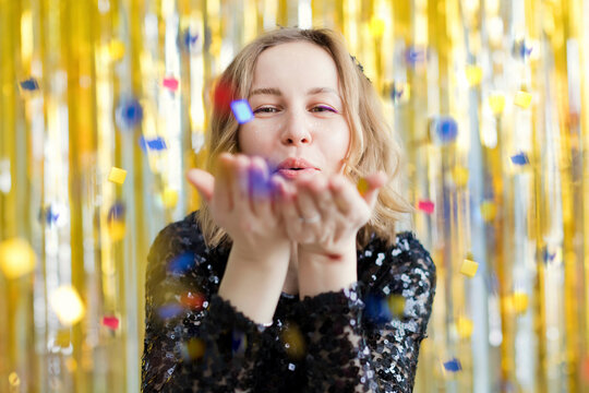 Woman wearing black dress blowing confetti in front of golden tinsel