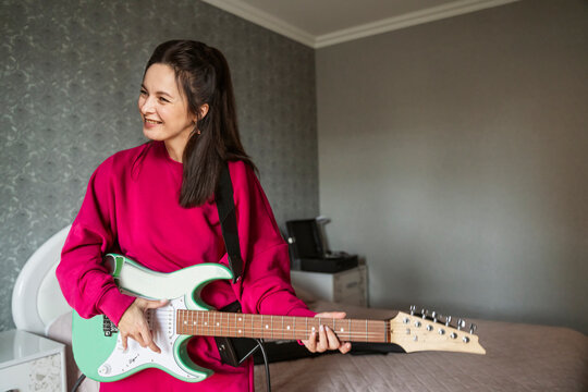 Smiling woman playing electric guitar in bedroom