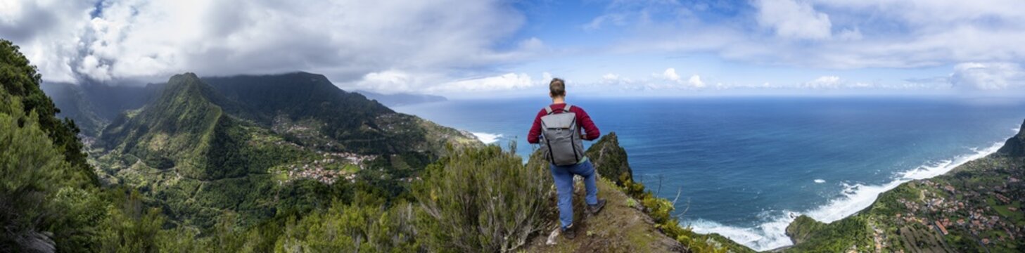 Hikers on the ridge of Pico do Alto, panorama, view of densely overgrown mountains and the village of Boaventura, view of the coast and sea with the village of Arco de Sao Jorge, Madeira, Portugal