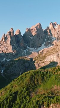 Dolomites rocky peaks vertical sunset alpenglow Italy Alps mountain landscape dramatic spires snow patches green forest slope travel nature slow motion adventure hiking scenic UNESCO