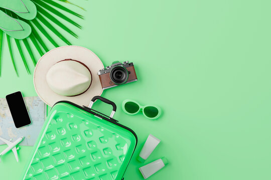 Green suitcase and travel accessories arranged on green background