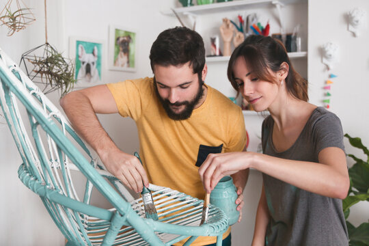 Young couple painting wicker armchair at home