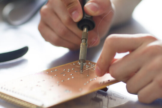 Electronic apprentice soldering circuit board at workshop, detail