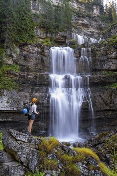 Young pretty hiker standing on rocks in front of Cascata di Mezzo waterfall, long exposure, Vallesinella, Brenta, Trentino, Italy