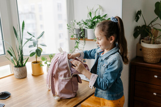 Smiling girl opening backpack on table at home