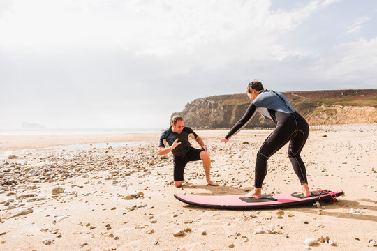 France, Bretagne, Crozon peninsula, man teaching woman surfing on beach