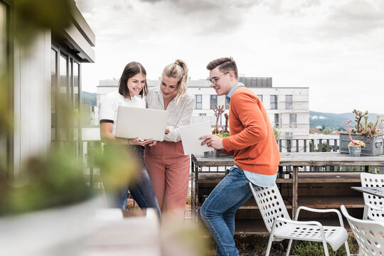 Casual business people with laptop meeting on roof terrace