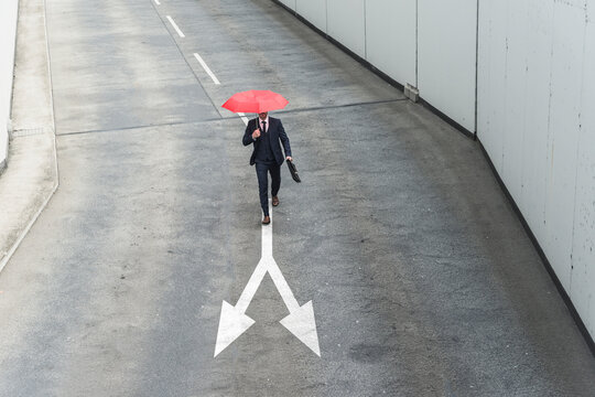 Businessman with red umbrella walking on road marking