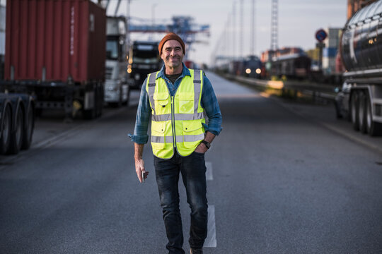 Smiling male truck driver with hand in pocket walking on street at dock