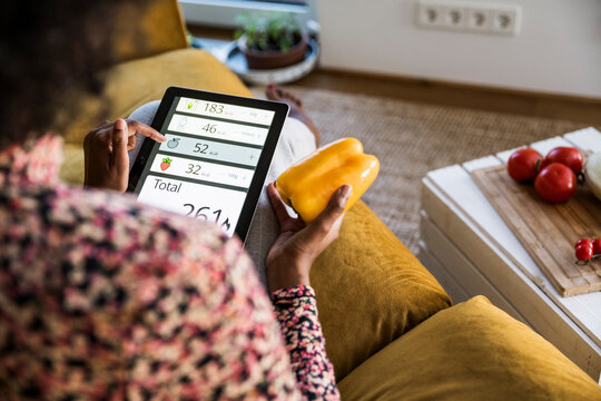 Person tracking calories on tablet holding yellow bell pepper