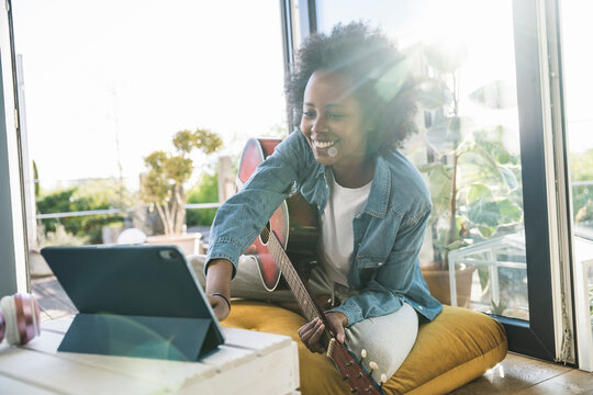 Woman learning to play guitar online with a tablet at home