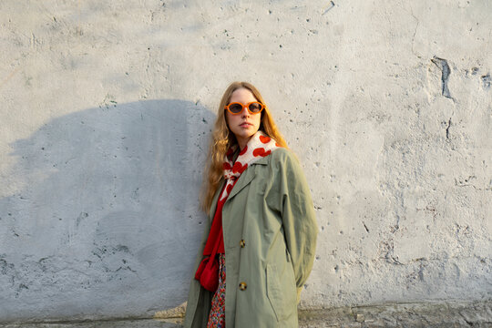 Woman in vintage clothing and sunglasses by a wall at sunset