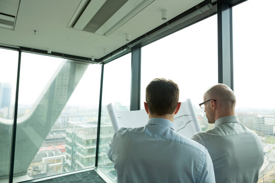 Two businessmen in office looking at blueprint