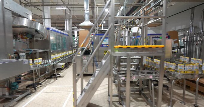 Cinematic tracking shot moving along an automated carton packaging line and conveyor belts in a modern food and beverage factory