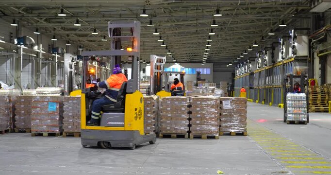 Steady wide shot of a busy modern industrial warehouse with workers operating yellow forklifts and moving pallets of goods