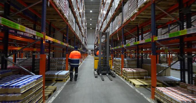 Cinematic tracking shot following a worker operating a yellow reach truck down a narrow aisle in a large distribution warehouse
