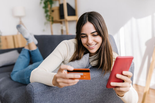 Happy woman with credit card doing shopping on smart phone at home