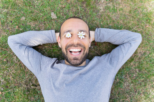 Smiling man lying on grass with flowers over eyes in spring