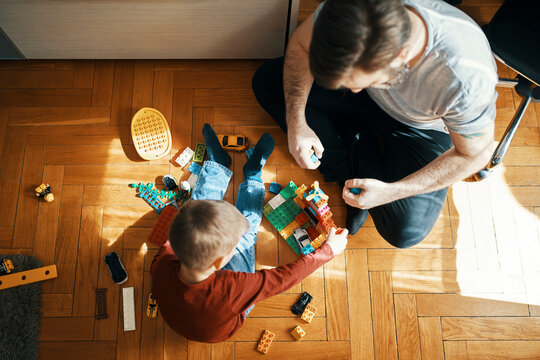 Father and son sitting on the floor playing together with building bricks, top view