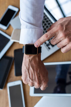 Close-up of a person pointing at a smartwatch among various devices.