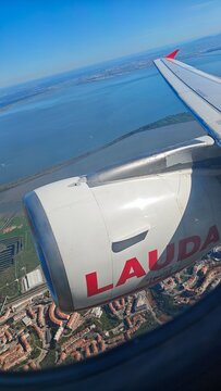 Lisbon, Portugal - March 30, 2026: Airplane wing featuring LAUDA logo and engine above a coastal area with water and urban structures visible below
