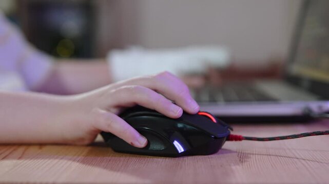 Child using wired computer mouse moving it across table, close up. Contrast of large computer equipment and small child hand. Computer use by generation alpha.