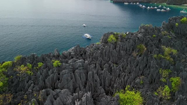 Aerial flypass of Twin Rocks sharp limestone cliffs revealing turquoise emerald bay with dozens of bangka tour boats in El Nido Palawan Philippines