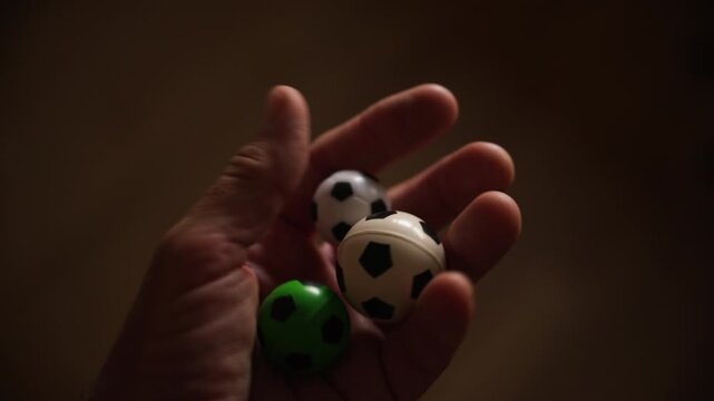 Close-up of hand gently holding three miniature soccer balls in warm, low light. The playful composition evokes childhood, nostalgia and love of sport and small-collection hobbies. 4K.