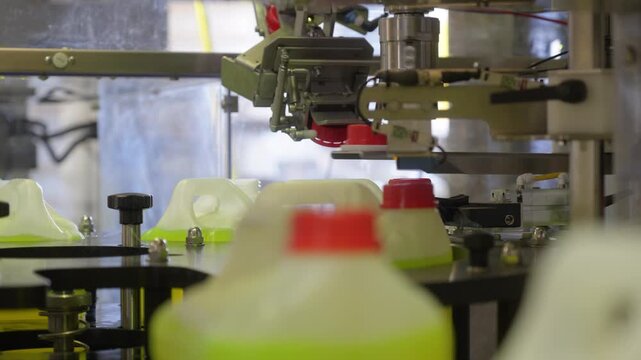 Automated capping head applies red caps to plastic chemical canisters moving on factory conveyor line