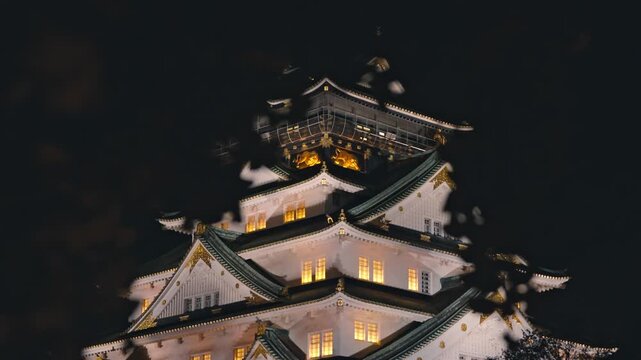 The majestic multi-tiered main keep of Osaka Castle beautifully illuminated against the dark night sky.