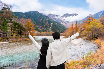 Naklejka premium Happy young couple tourist relaxing and enjoying with beautiful nature autumn foliage at kamikochi in Japan