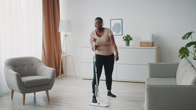 Happy Black Woman Engaging In Cleaning With Mop In Bright Modern Living Room, Smiling And Enjoying Tidying Up. Home Setting Emphasizing Cleanliness And Organization, Home Cleaning Concept.