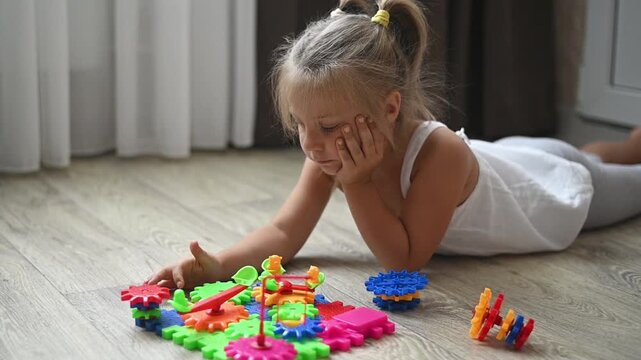 Child engaged in assembling bright plastic gears into structure, sitting on floor. toy fosters coordination, cognitive skills, and creative thinking, ideal for childhood development activities.