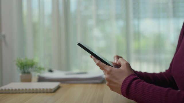 Close up view of woman's hands typing and scrolling on a tablet. Businesswoman working with a digital device at her office desk