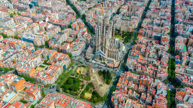 Aerial drone view of the Sagrada Familia basilica under construction surrounded by the Eixample district grid layout in Barcelona, Catalonia, Spain during the daytime.