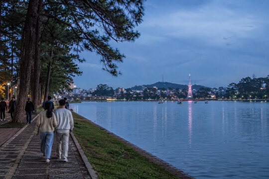 Two travelers walking along Da Lat lakeside promenade with pine trees.generative AI