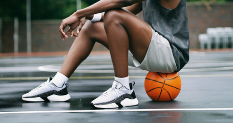 Naklejka premium Man, legs and sneakers with basketball on court for outdoor game, match or sports practice. Male person, athlete or player rest on ball for training break, competition or exercise on urban pitch