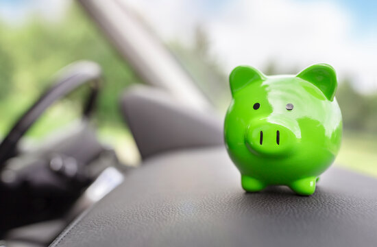 Green piggy bank money box inside car, vehicle purchase, maintenance, insurance or driving and motoring cost