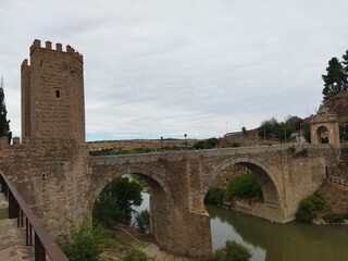 Obraz premium Puente de piedra medieval con torre defensiva sobre un río bajo un cielo nublado