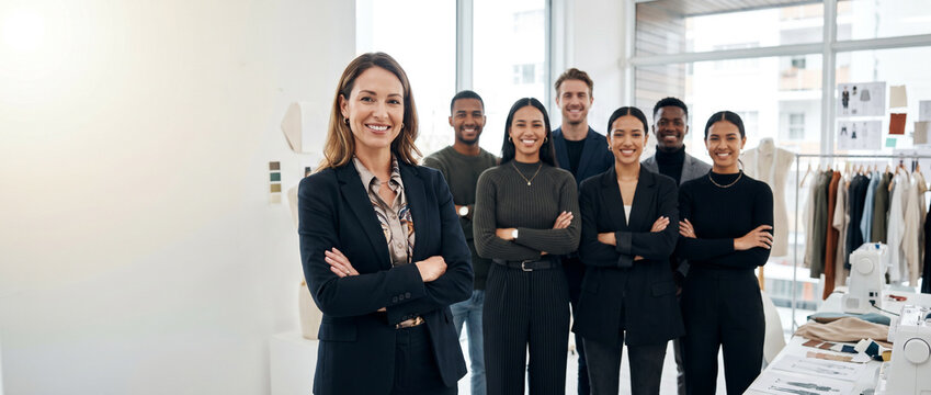Diverse fashion professionals in modern design studio, led by confident female designer, creative team standing together with clothing racks, fabrics, and studio workspace in background.