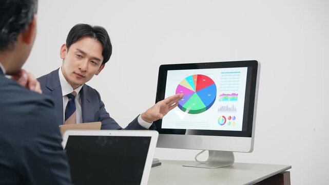 PC画面を見ながら説明するビジネスパーソン