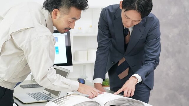 カタログを見ながら会議するビジネスパーソンと作業員のグループ