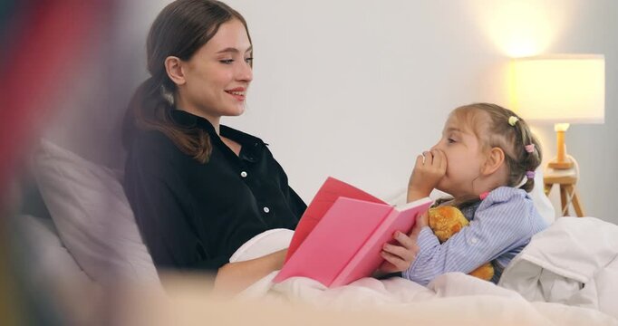 Happy mother reading a storybook to her little daughter in bed.
