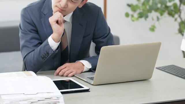 オフィスで仕事をしながら悩む男性ビジネスパーソン